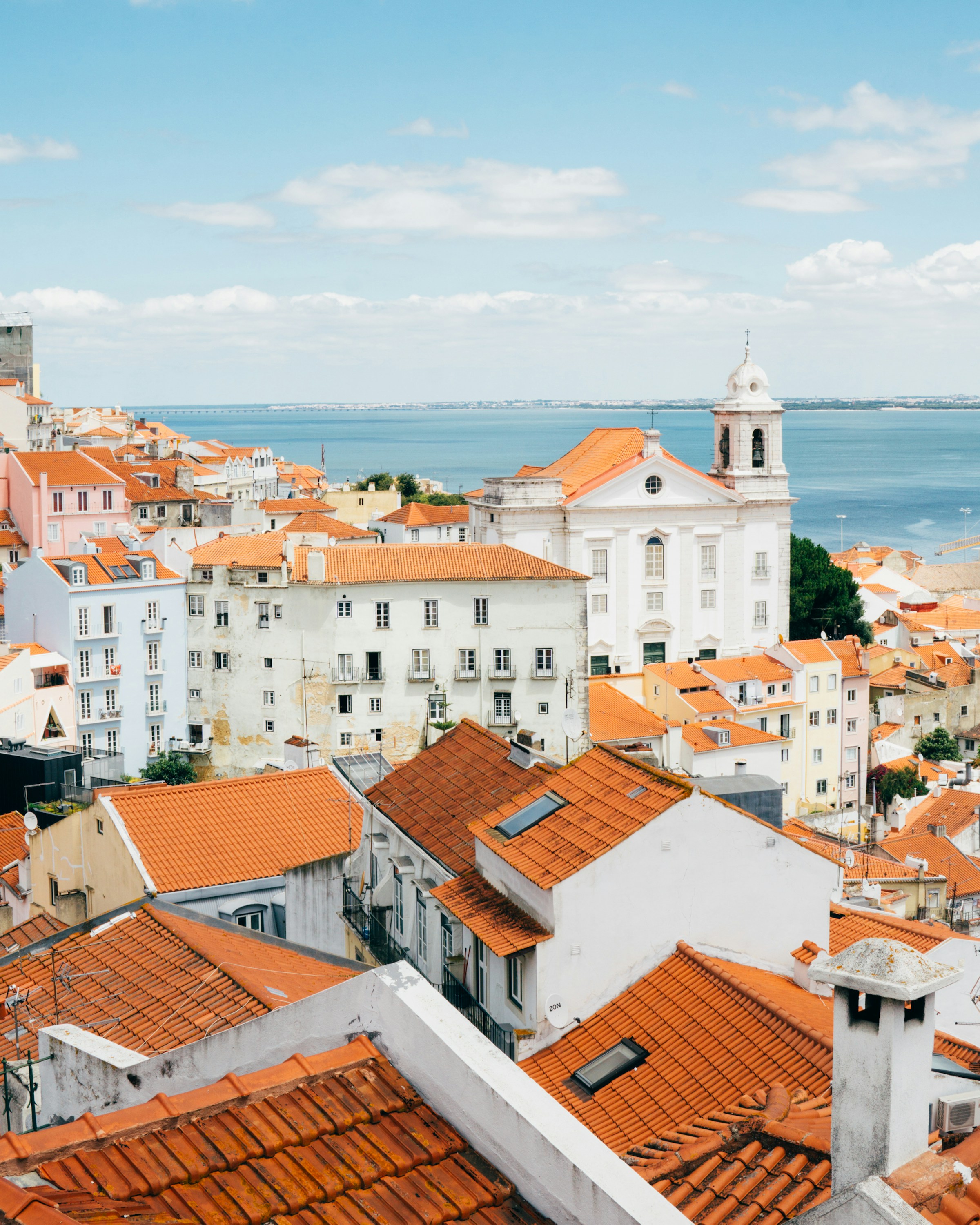 Rows of orange-tiled rooftops above the water in Lisbon, Portugal